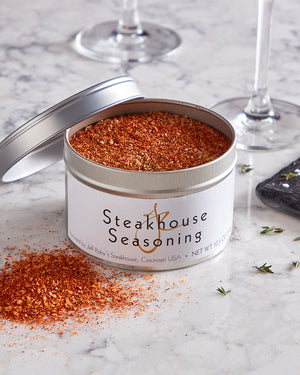 Open container of Jeff Ruby's steakhouse seasoning on a marble surface with glasses in the background.