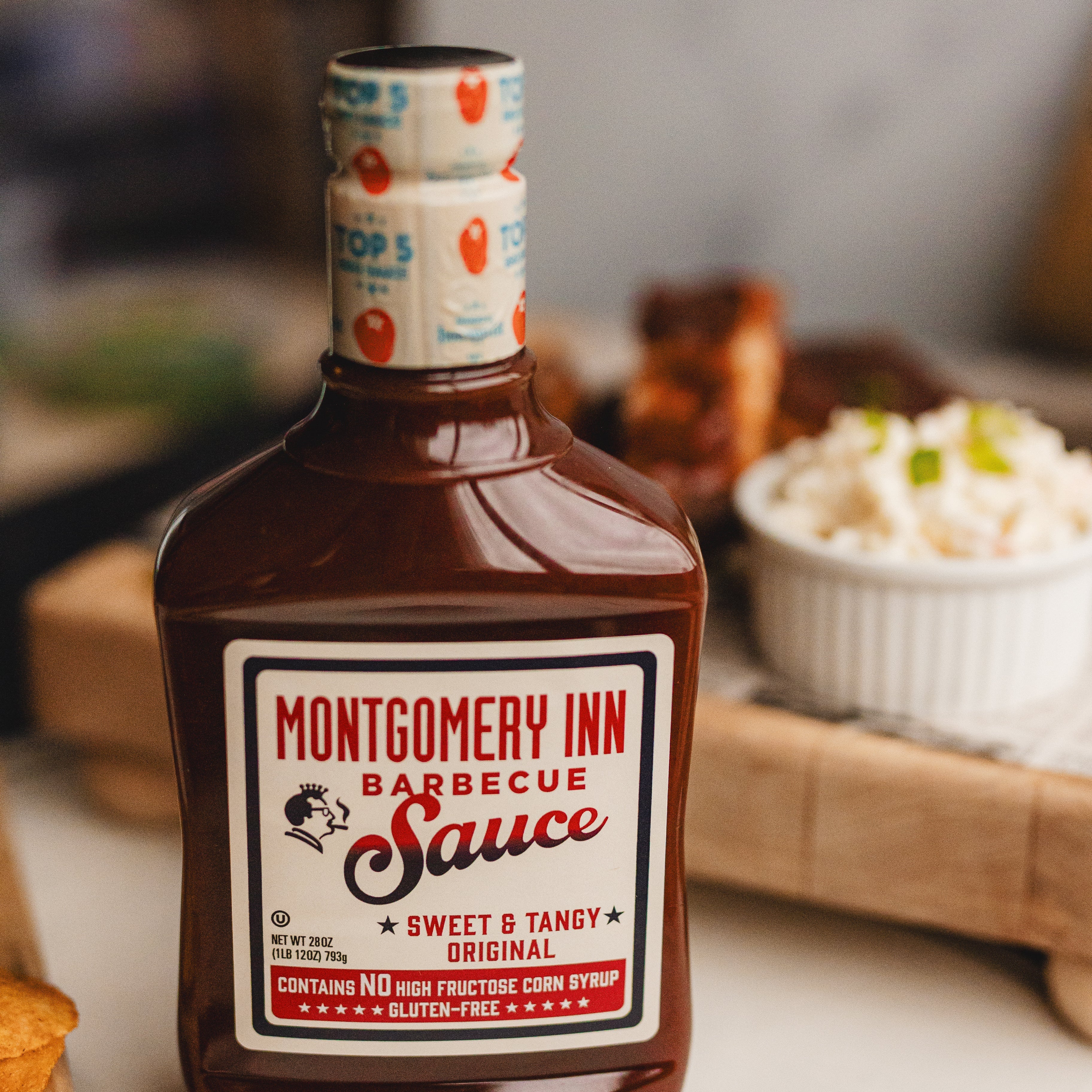 Bottle of Montgomery Inn Barbecue Sauce on a table with food in the background